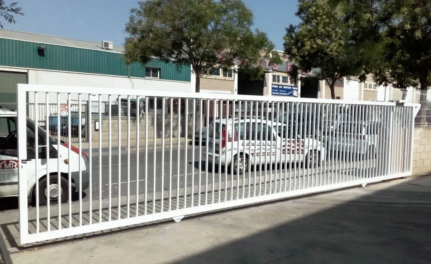 Puerta de seguridad corrediza de metal blanco que protege vehículos estacionados.
