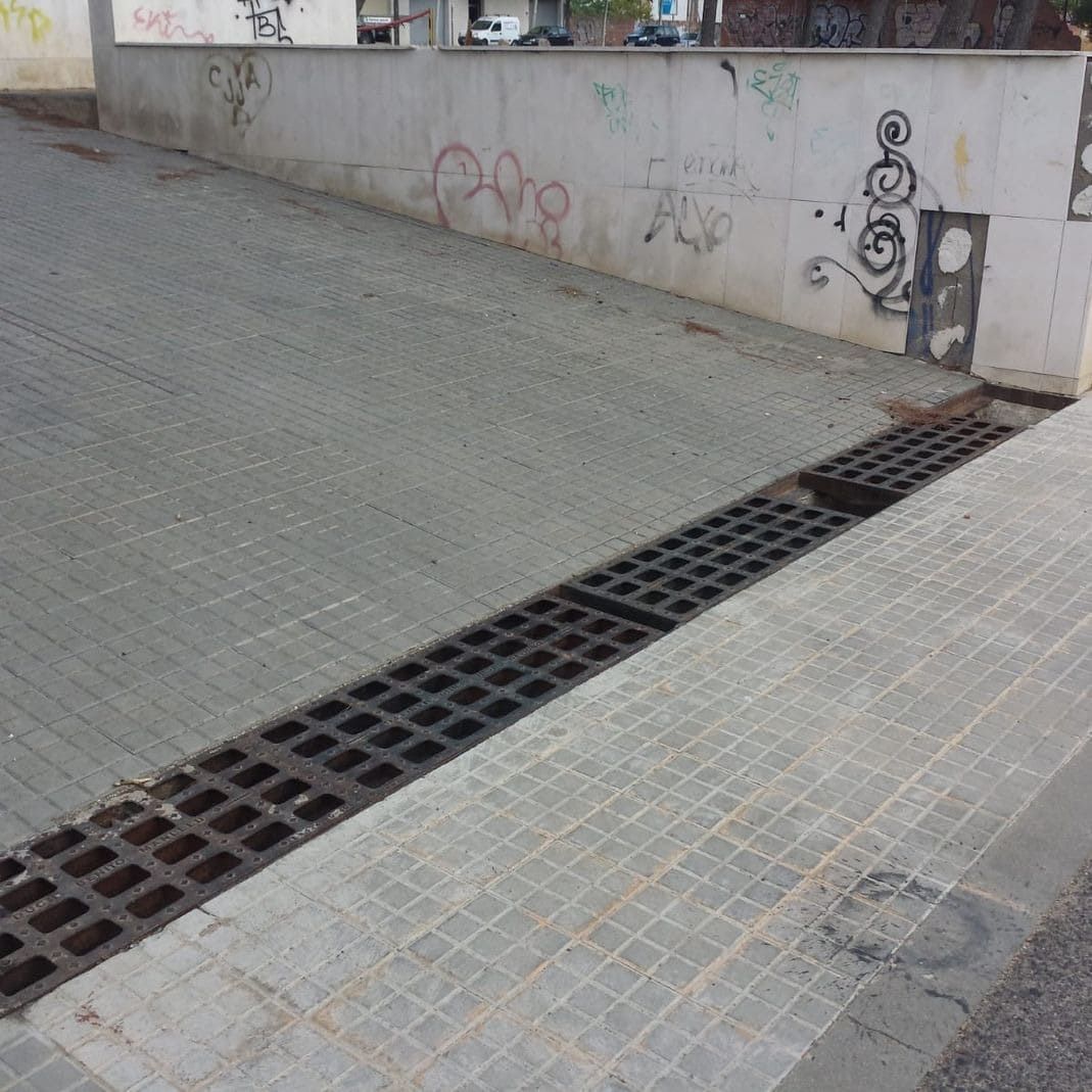 Rampa de hormigón con desagüe enrejado que conduce a una pared con grafitis.