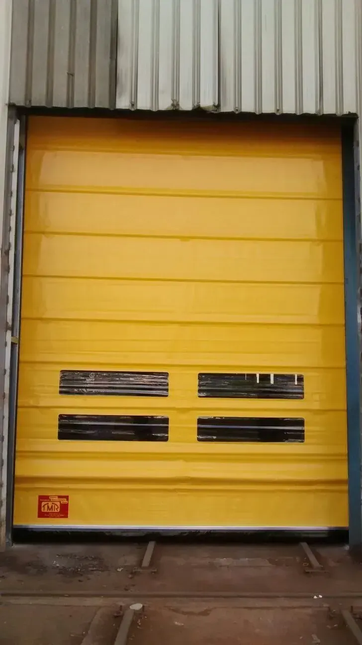 Puerta enrollable industrial amarilla con rejillas de ventilación negras, cerrada. En un almacén.