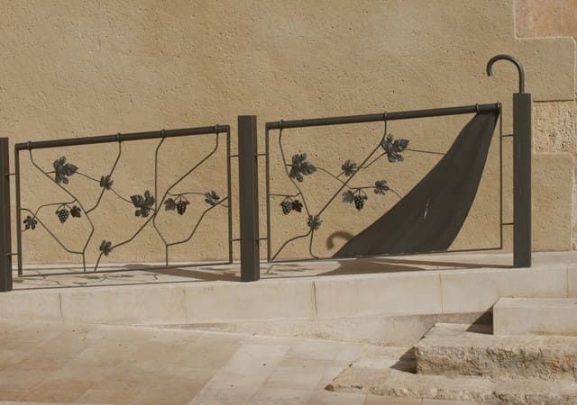 Valla de hierro forjado con diseño de vid, fijada a unos escalones de piedra junto a un edificio.