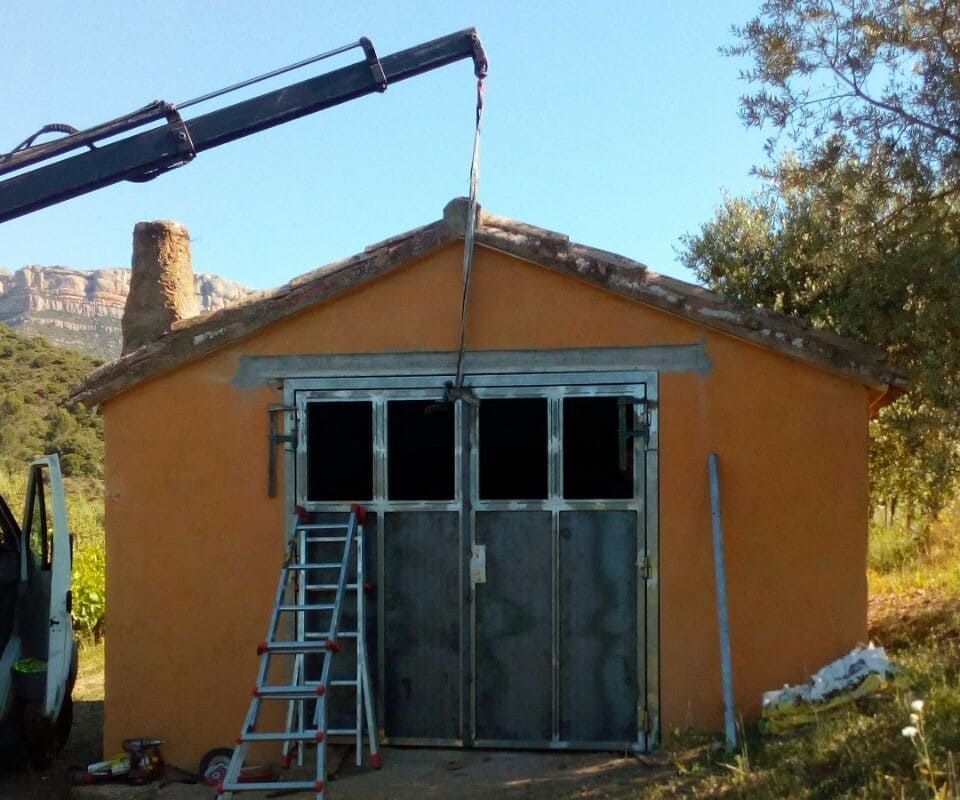 Edificio naranja con puertas de metal, una grúa encima y una escalera, probablemente en construcción.
