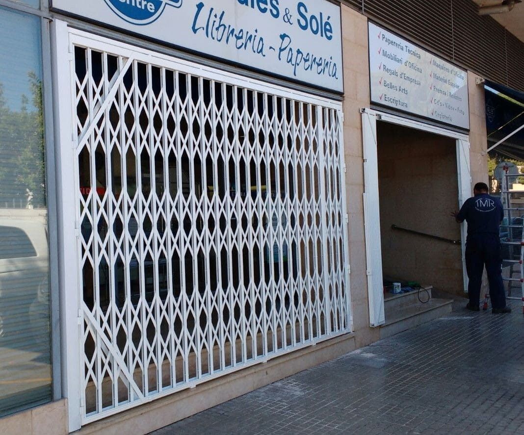 Puerta de seguridad blanca frente a una tienda. Se ve a una persona con ropa oscura en el umbral.
