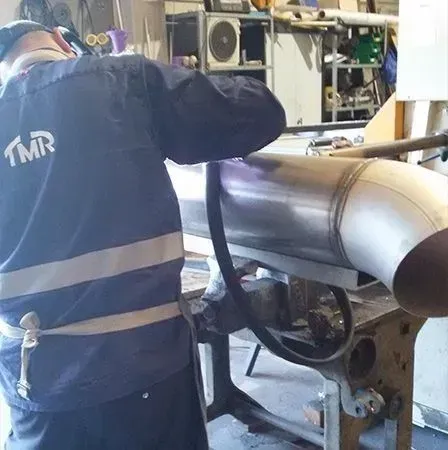 Persona con ropa de trabajo azul soldando un tubo de metal en un taller.
