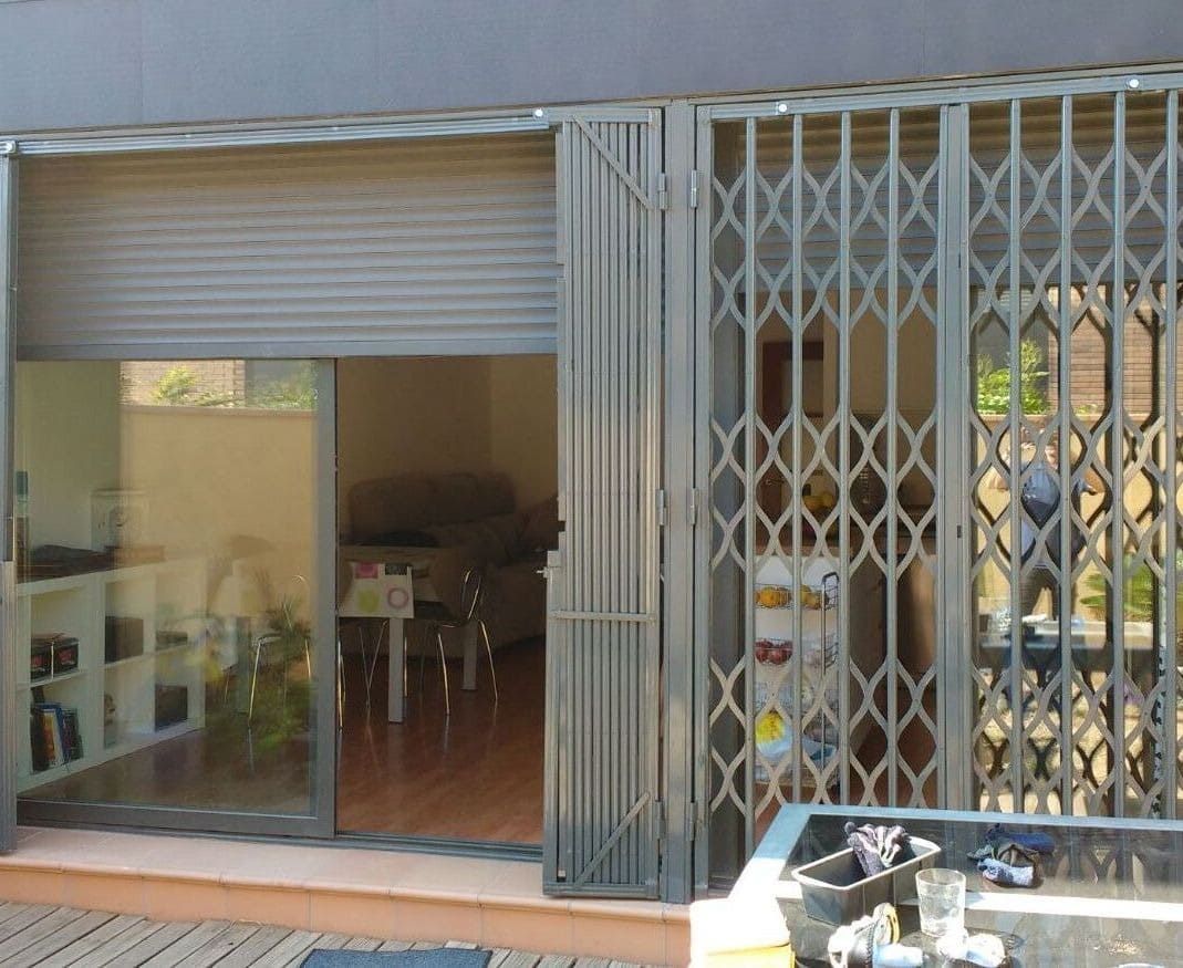 Vista exterior con puertas corredizas de vidrio, portón de seguridad retráctil y persiana enrollable cerrada.