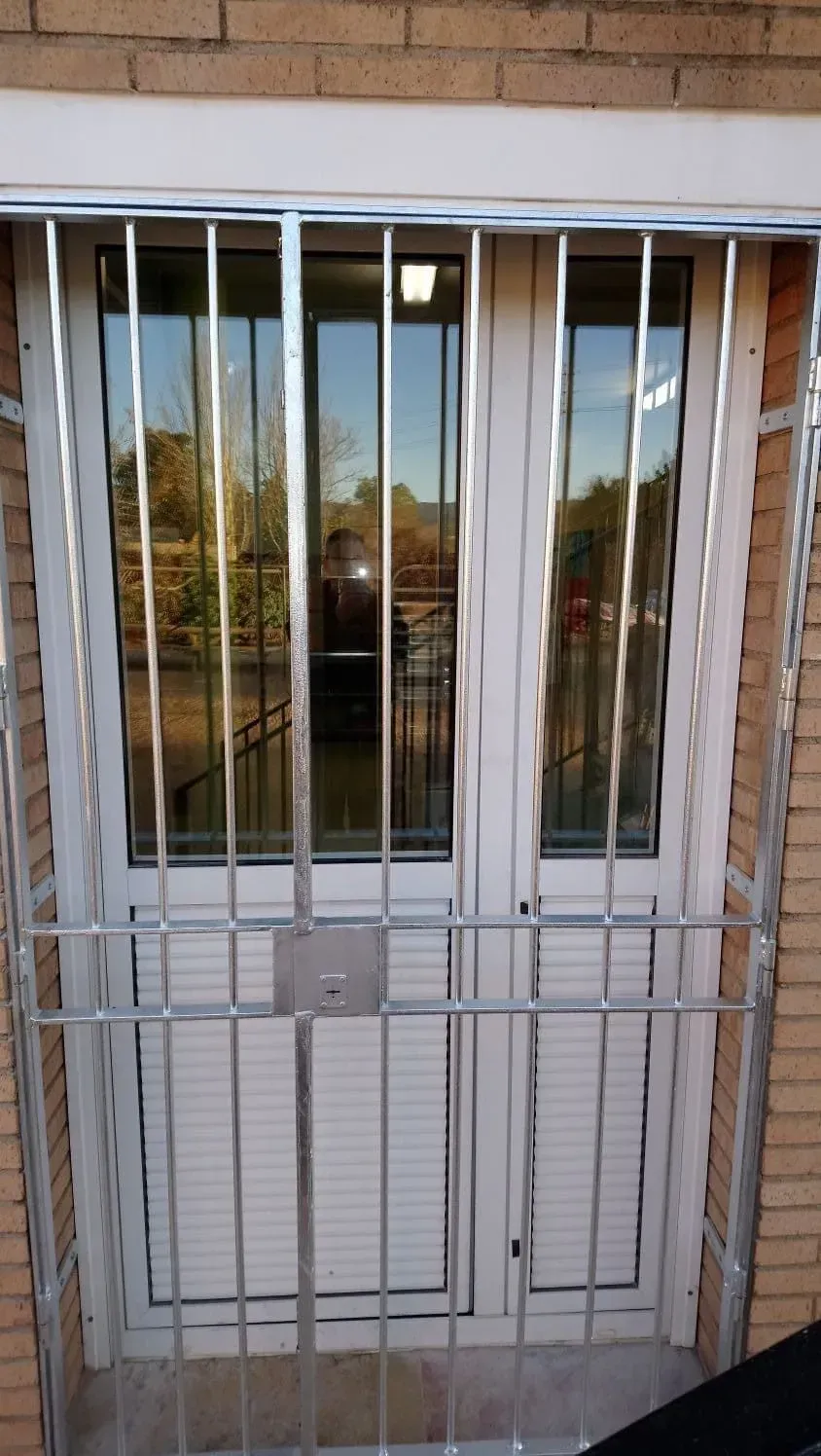 Puertas dobles blancas con rejas de seguridad metálicas.