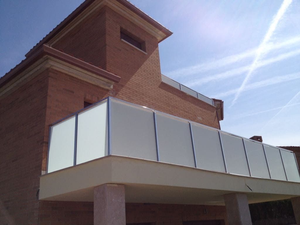 Balcón con paneles blancos y un edificio de ladrillo contra un cielo brillante.