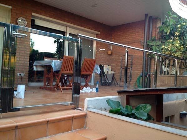 Patio con barandilla de vidrio, pared de ladrillo, mesa de comedor y sillas.