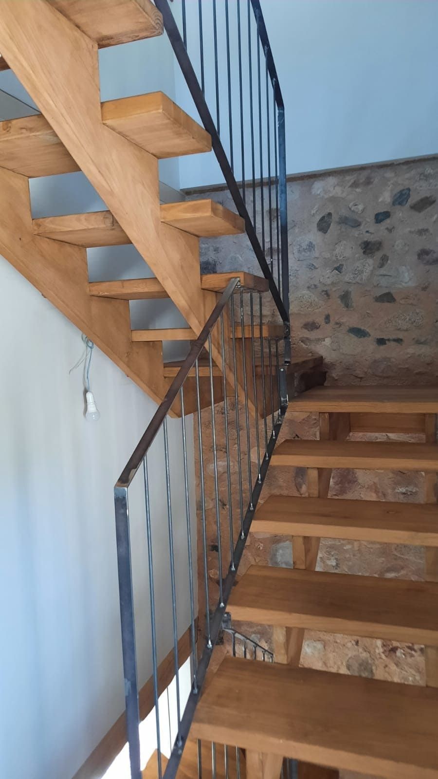 Escalera de madera con barandilla de metal negro en un edificio de piedra y paredes blancas.