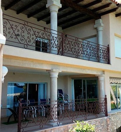 Edificio beige de dos pisos con balcones, barandillas de hierro marrón ornamentadas.