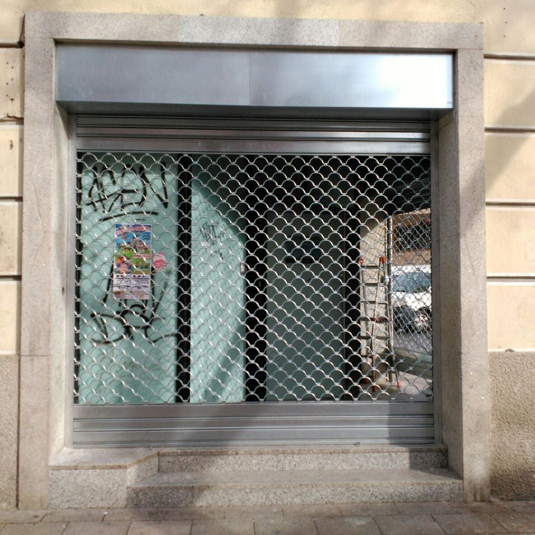 Fachada de local cerrado con reja de seguridad y grafitis en el cristal, enmarcado en piedra.
