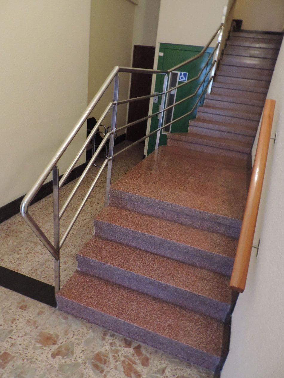 Escalera con escalones marrones moteados, pasamanos de acero inoxidable y pasamanos de madera. 