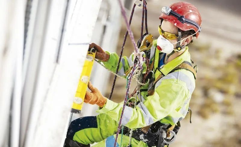 Trabajador con equipo de seguridad en un edificio, utilizando un nivel.