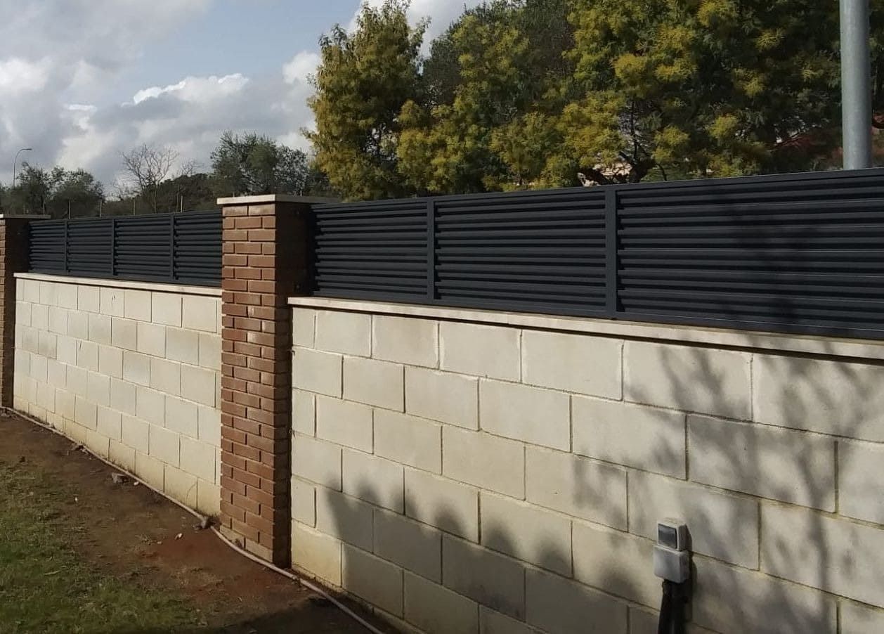 Una pared de bloques de hormigón gris con una valla de listones de color gris oscuro en la parte superior.