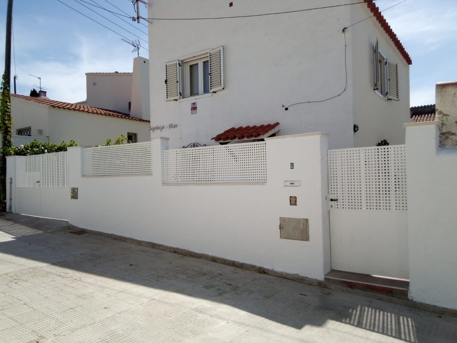 Casa de estuco blanco con valla y puerta blancas en una calle soleada.