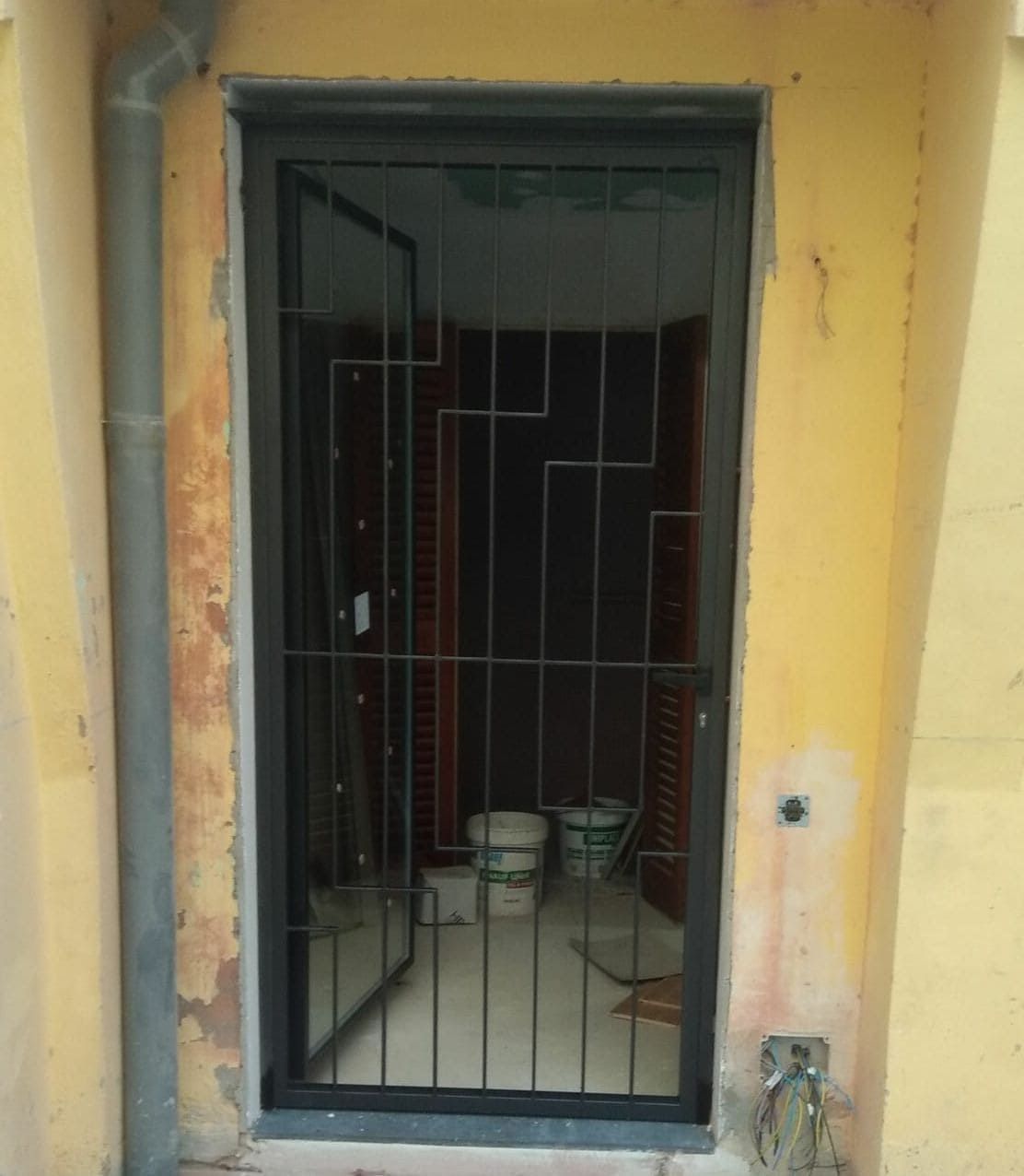 Puerta de seguridad negra con rejas sobre el marco de la puerta, con un vistazo al interior. El exterior es amarillo.