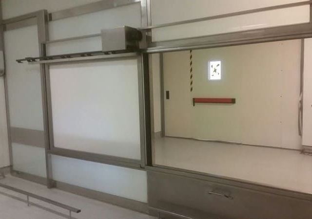 Puertas corredizas en una pared blanca en un entorno similar a un hospital con un pasillo visible.