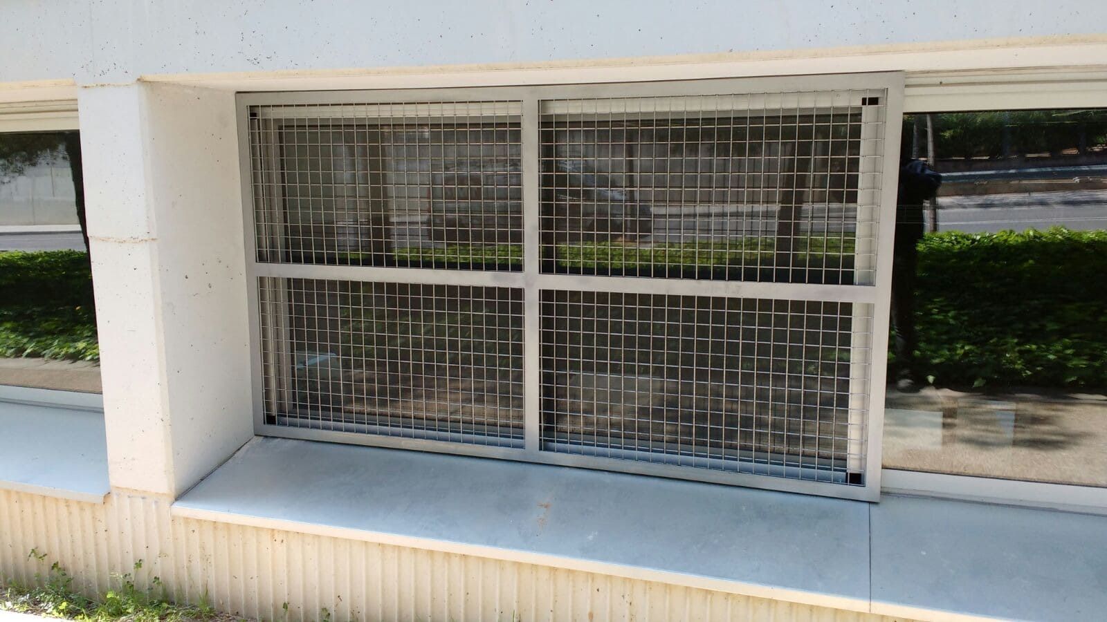 Ventana con rejas de seguridad, marco blanco, rejas grises, ambiente exterior.