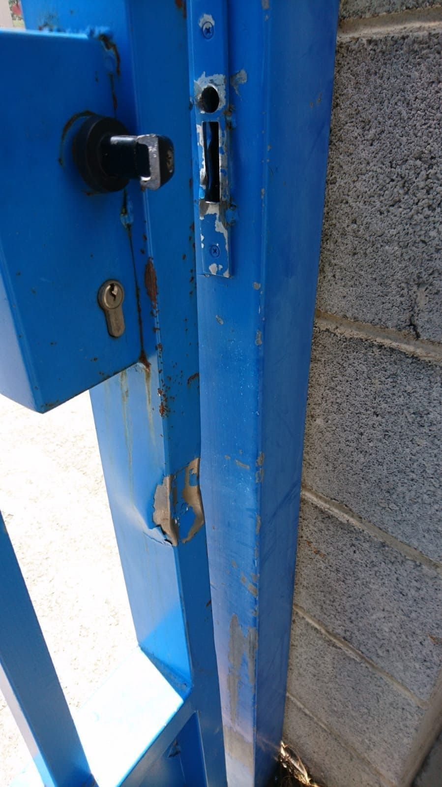 Puerta metálica azul con cerradura con llave y pestillo, fijada a una pared de ladrillos.