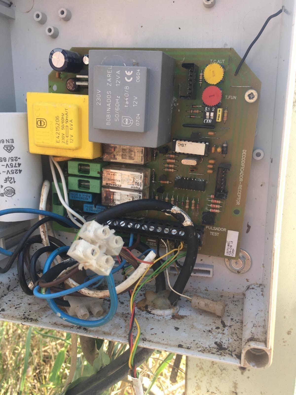 Placa de circuito con diversos componentes dentro de una carcasa blanca. Se ven los cables y los bloques de terminales.