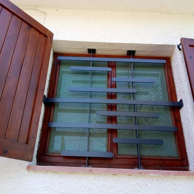 Ventana con contraventanas de madera y reja de seguridad metálica de color negro.