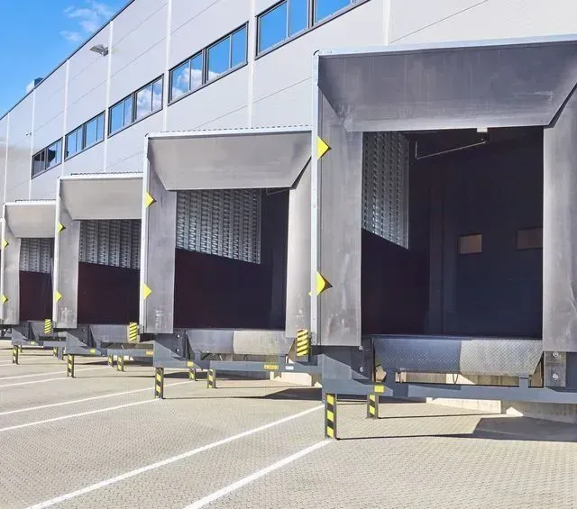 Muelles de carga de un edificio de almacén, con bahías abiertas, acentos grises y amarillos.