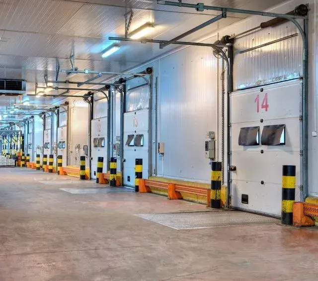 Muelle de carga con múltiples puertas blancas cerradas, parachoques y luces superiores.