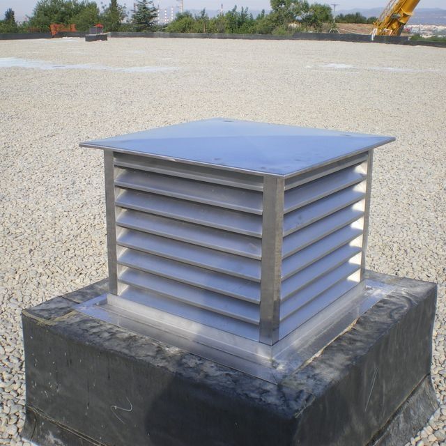 Respiradero metálico cuadrado sobre azotea, con lamas horizontales y parte superior plana, rodeado de grava.