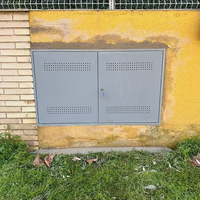 Puertas metálicas grises empotradas en una pared amarilla, junto a una sección de ladrillo.