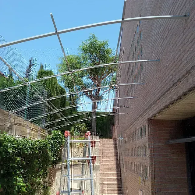 Andamio y estructura metálica fijados a un edificio de ladrillo, sobre una escalera con una valla de alambre a la izquierda.
