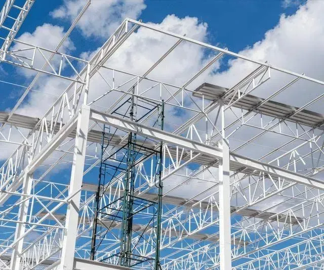 Estructura de acero blanco bajo un cielo azul parcialmente nublado, con andamios en el medio.