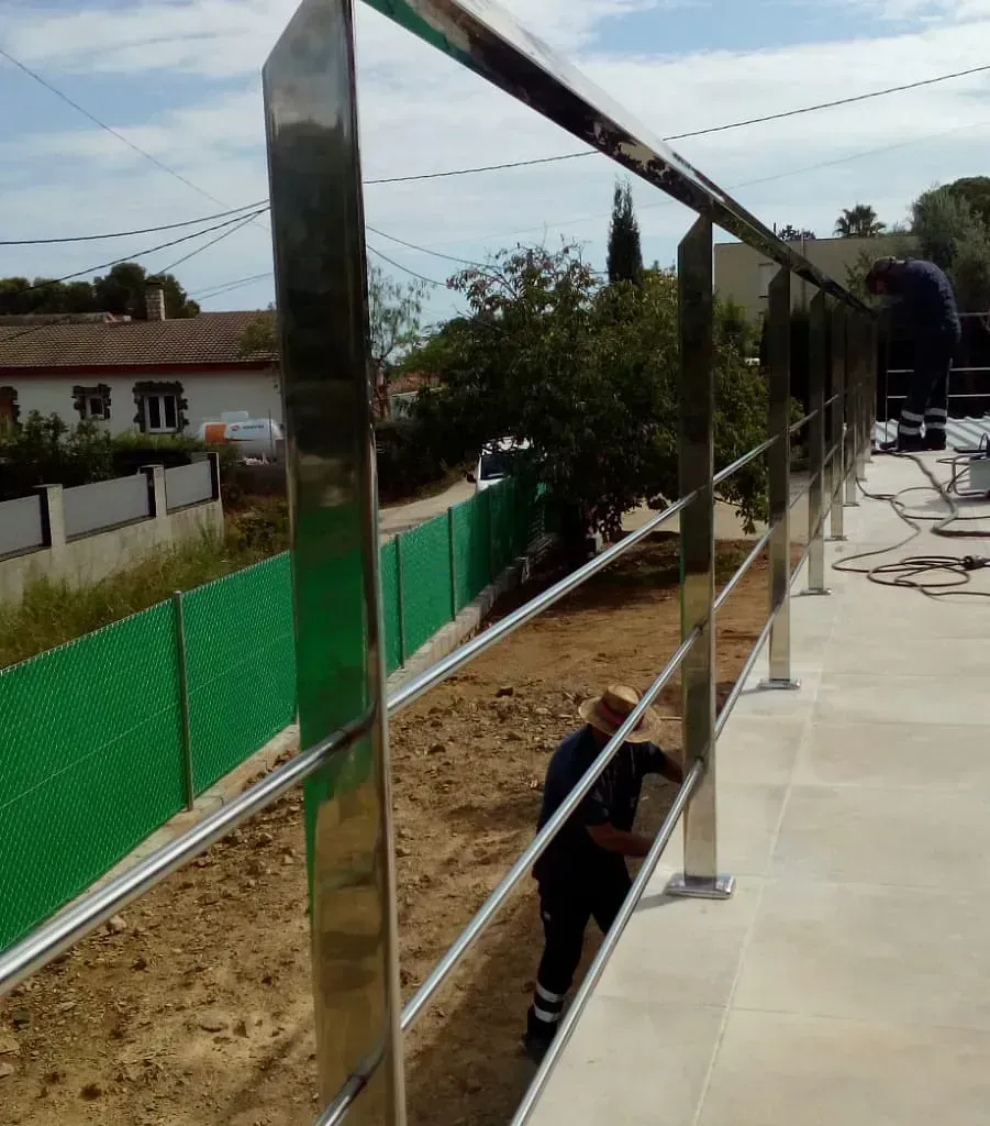 Barandilla de acero inoxidable siendo instalada al aire libre con los trabajadores a la vista.