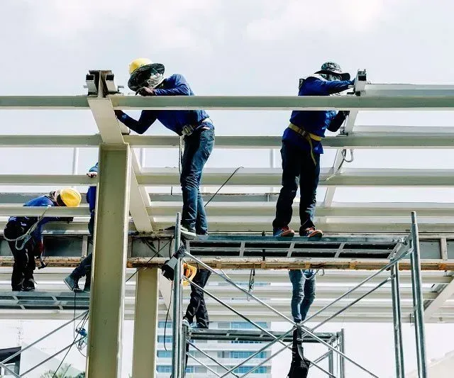 Obreros de la construcción soldando vigas de acero en un andamio, a plena luz del día.