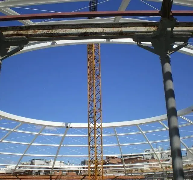 Vista del sitio de construcción a través de una estructura de cúpula; grúa amarilla contra un cielo azul.