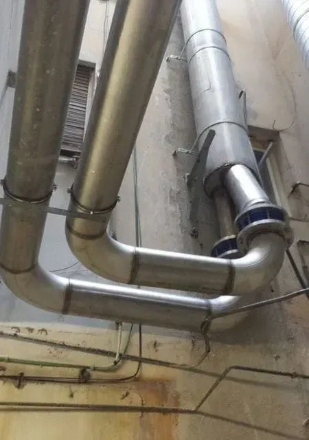 Tubos y conductos de metal fijados a una pared exterior desgastada con soportes y costuras de soldadura.