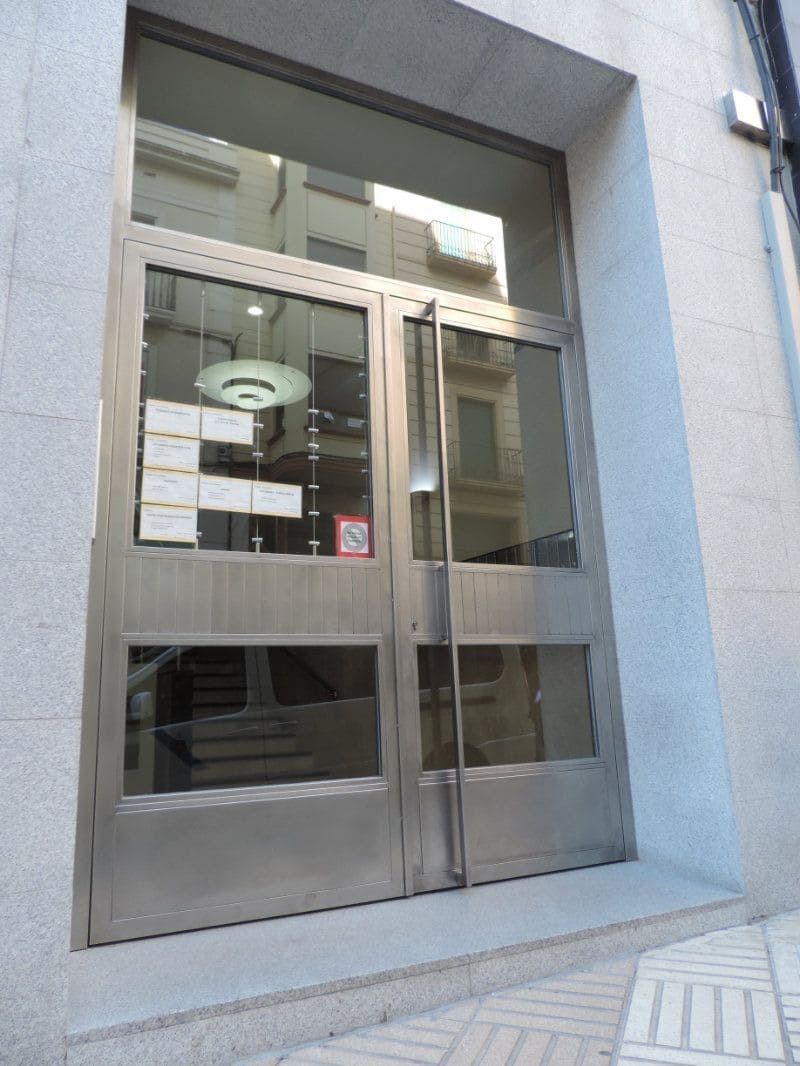 Puertas dobles de acero inoxidable con grandes paneles de vidrio, insertadas en una fachada de piedra.