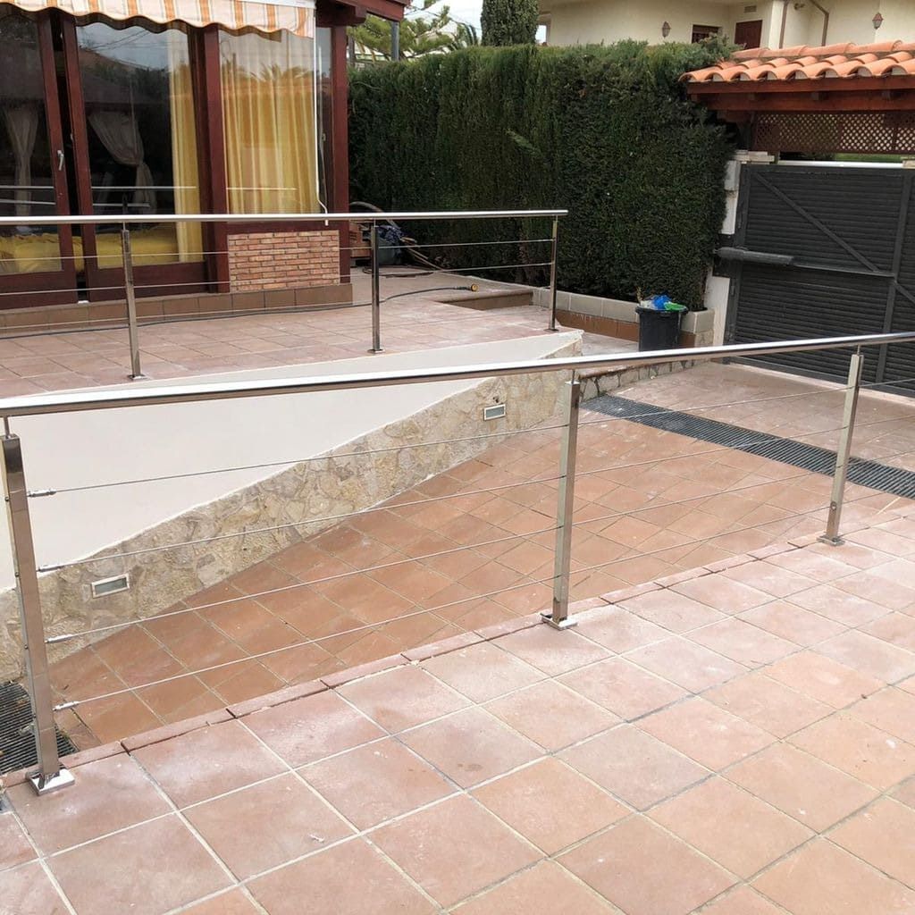 Una barandilla de acero inoxidable bordea un patio de baldosas, proporcionando seguridad en una zona hundida.