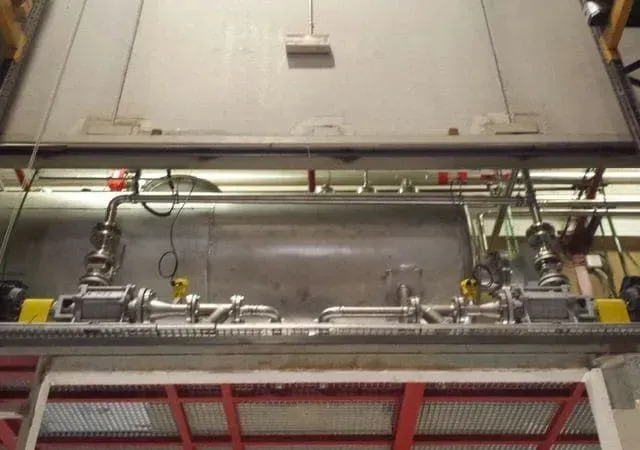 Gran tanque industrial con tuberías y válvulas dentro de un edificio.