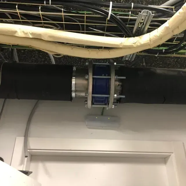 Sección de tubería aislada de color negro conectada mediante acoplamiento azul y plateado debajo de los cables.