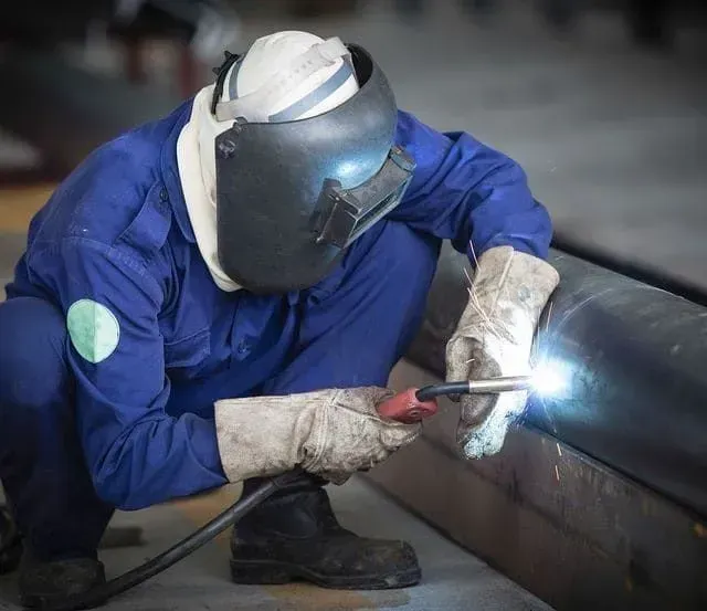 Soldador con mono azul y casco, soldando una tubería grande, en el interior.