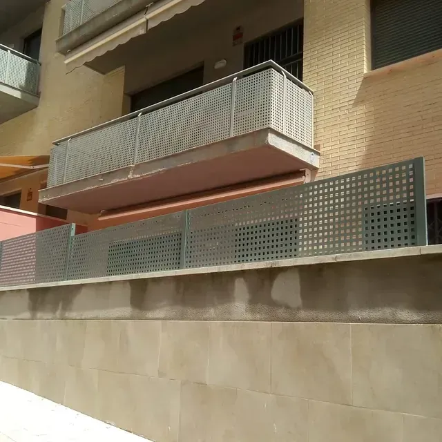 Balcón y valla de metal gris en el exterior de un edificio de color beige.