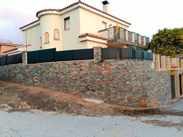 Casa de dos plantas con muro de piedra y reja metálica negra.
