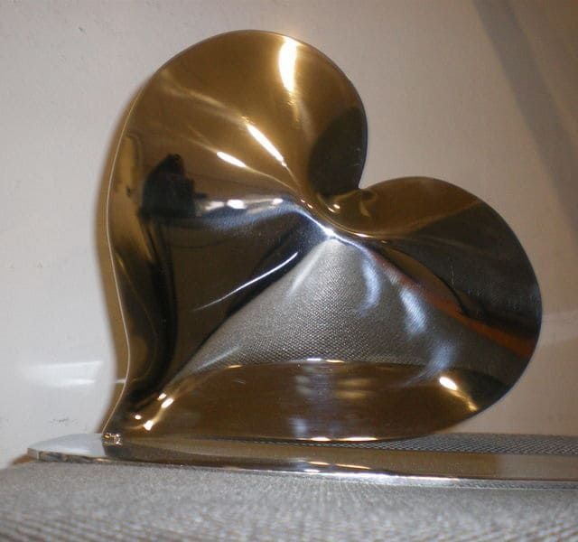 Escultura brillante, metálica, en forma de corazón, posiblemente de acero inoxidable.