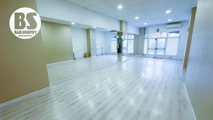 Espacio de oficina amplio y luminoso, con suelos blancos, paredes beige y grandes ventanales en la fachada
