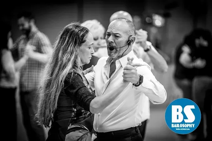Una pareja bailando, vestida de gala y muy junta, en una escena de salón de baile en blanco y negro.