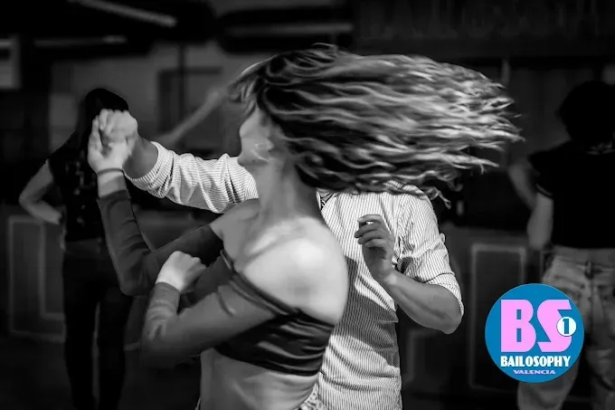 Foto en blanco y negro de dos personas bailando; una de ellas está en pleno movimiento de cabello, en un estudio o club