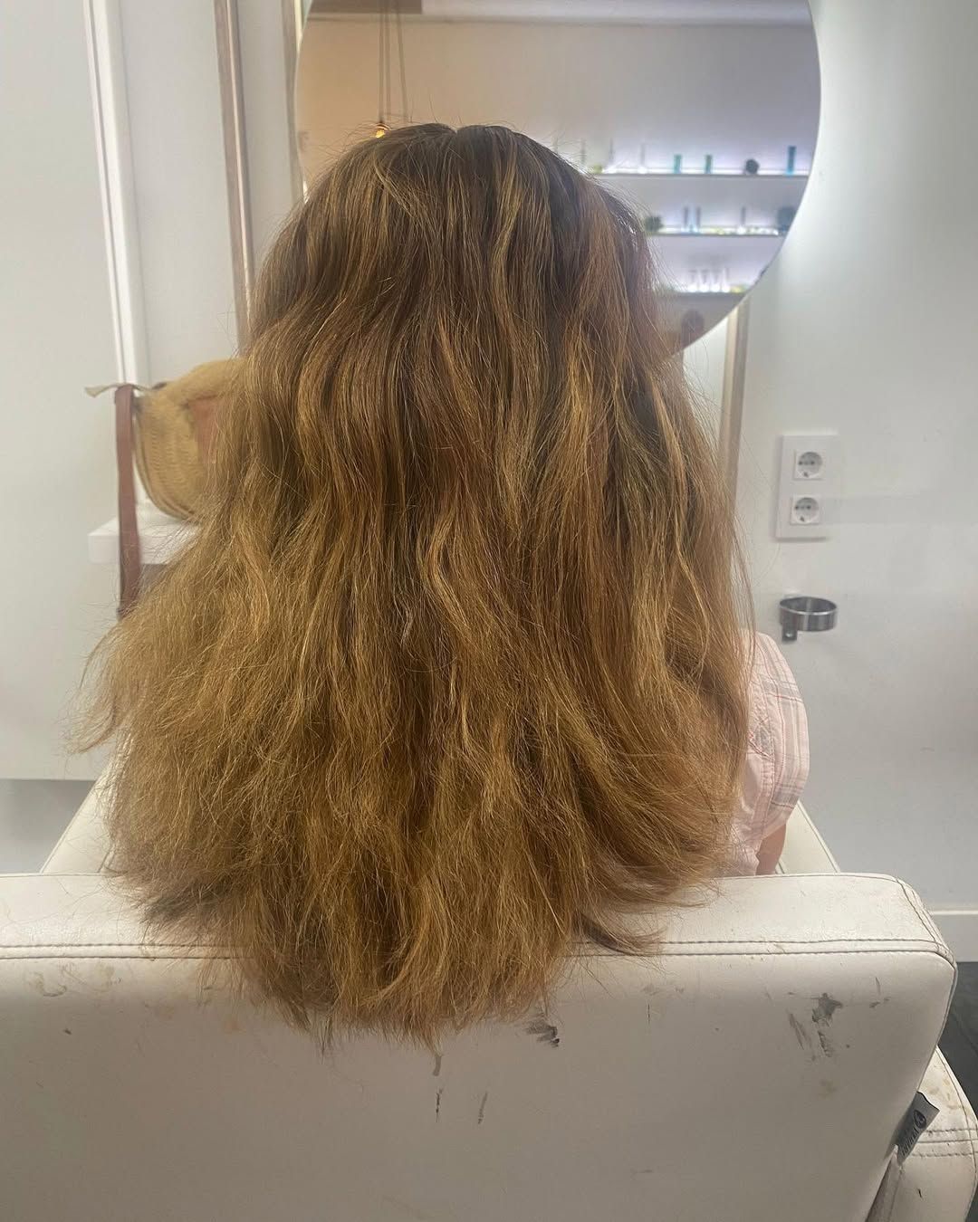 Persona con cabello castaño largo y ondulado vista de espaldas en el espejo del baño.