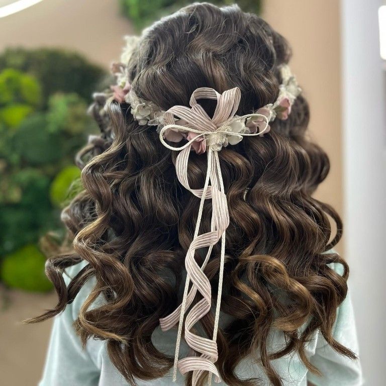 Vista posterior de cabello rizado oscuro con un delicado accesorio floral en forma de cinta.