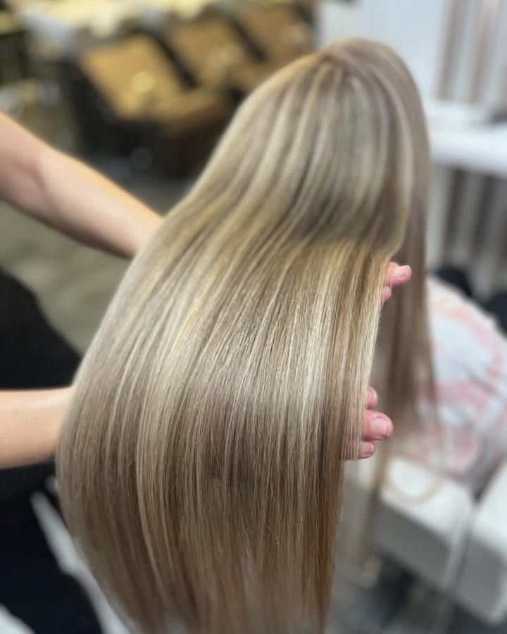 Cabello rubio largo y liso sostenido para mostrar su brillo y capas en un entorno de salón de belleza.
