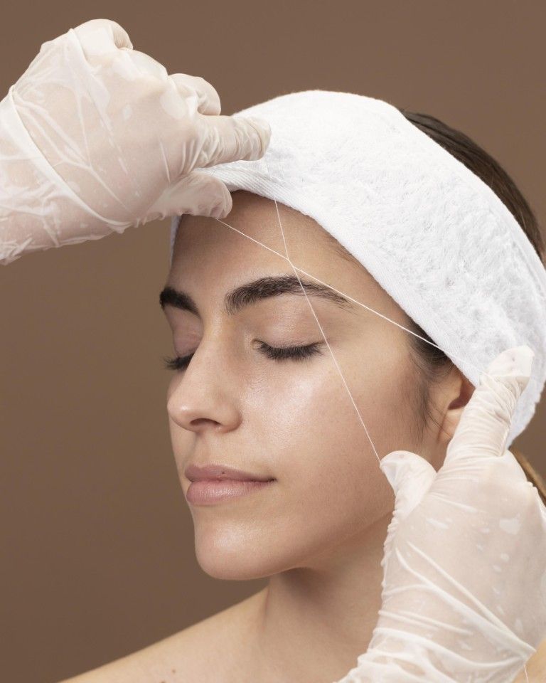 Manos enguantadas aplicando una mascarilla facial blanca en el rostro de una mujer.