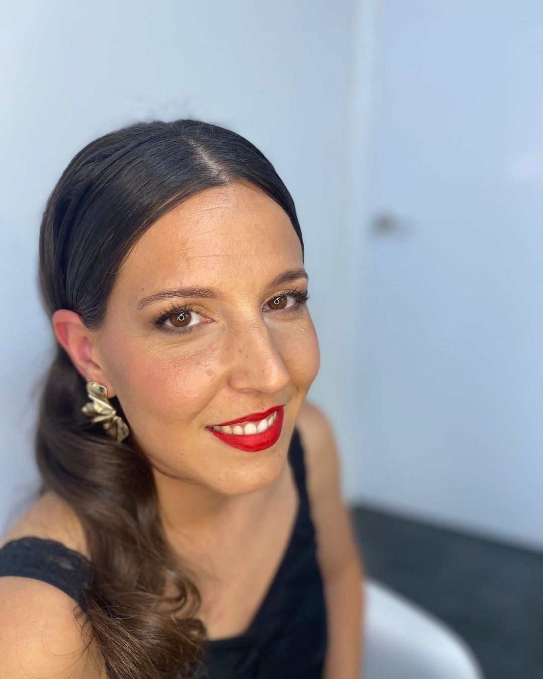 Primer plano de una mujer de cabello oscuro vestida de negro, con maquillaje dorado en los ojos, mirando hacia abajo.